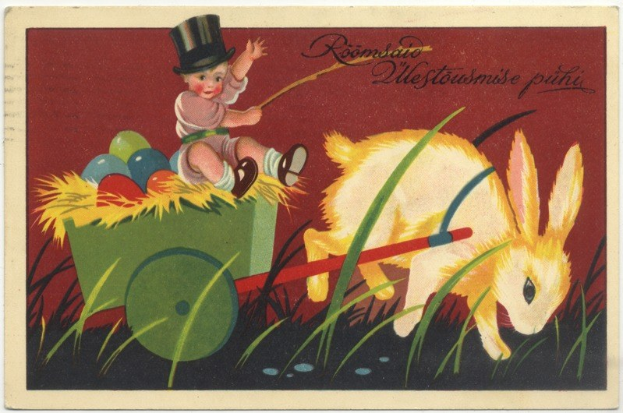 Alte Postkarte mit einem Baby in einem Zylinder, das einen Karren voller bunter Ostereier schiebt, begleitet von einem Kaninchen, mit handgeschriebener Ostergrüßtext.