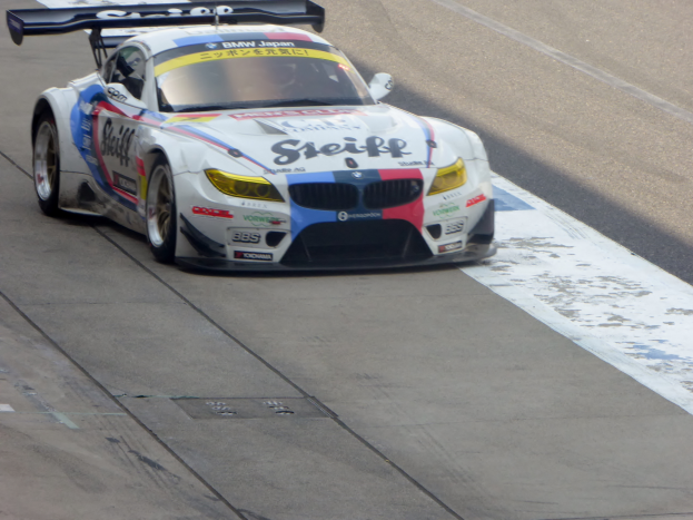 Ein BMW Z4 GT3-Rennwagen in strahlendem Blau und Weiß fährt auf einer Rennstrecke, zeigt seine schlank, aerodynamische Form mit niedrigem Profil, breiter Stand und großen, glänzenden Rädern.