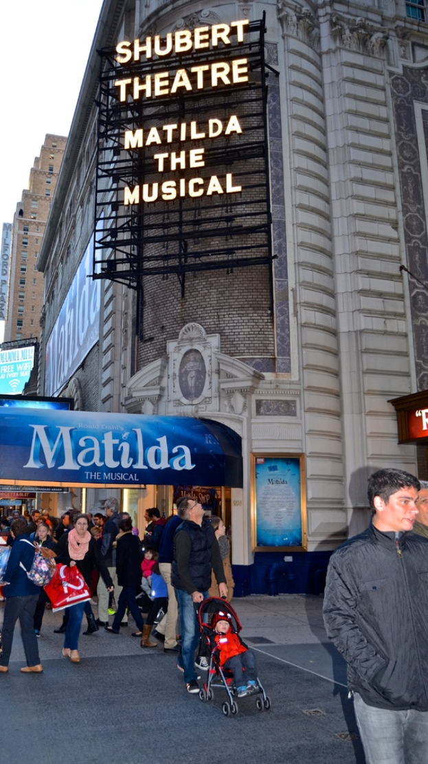 Eine Gruppe von Menschen in der Nähe von Gebäuden und Plakaten mit einem Baby im Kinderwagen.