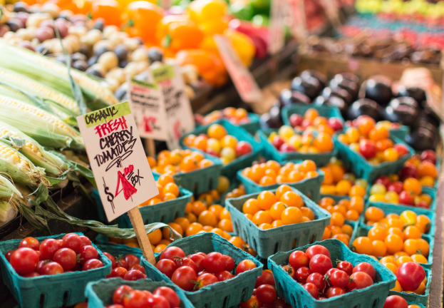 Ein Bauernmarkt mit Körben voller frischer Produkte wie Tomaten und Mais sowie Schilder im Hintergrund.