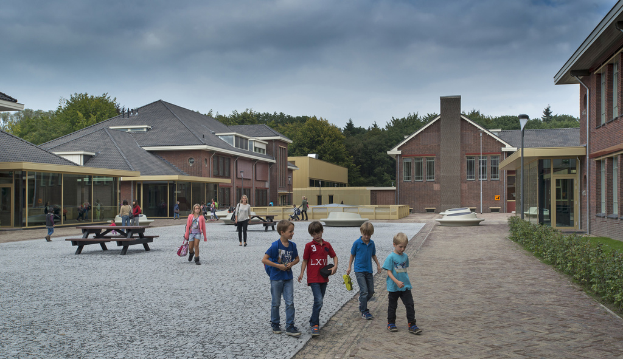 Eine Gruppe von Kindern und Frauen auf einem Weg umgeben von Häusern, Bäumen und einem bewölkten Himmel.