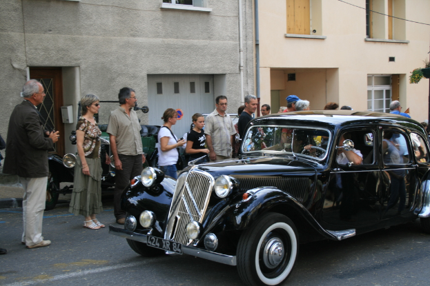 Ein Auto fährt auf einer Straße mit Menschen auf der linken Seite und Gebäuden im Hintergrund.