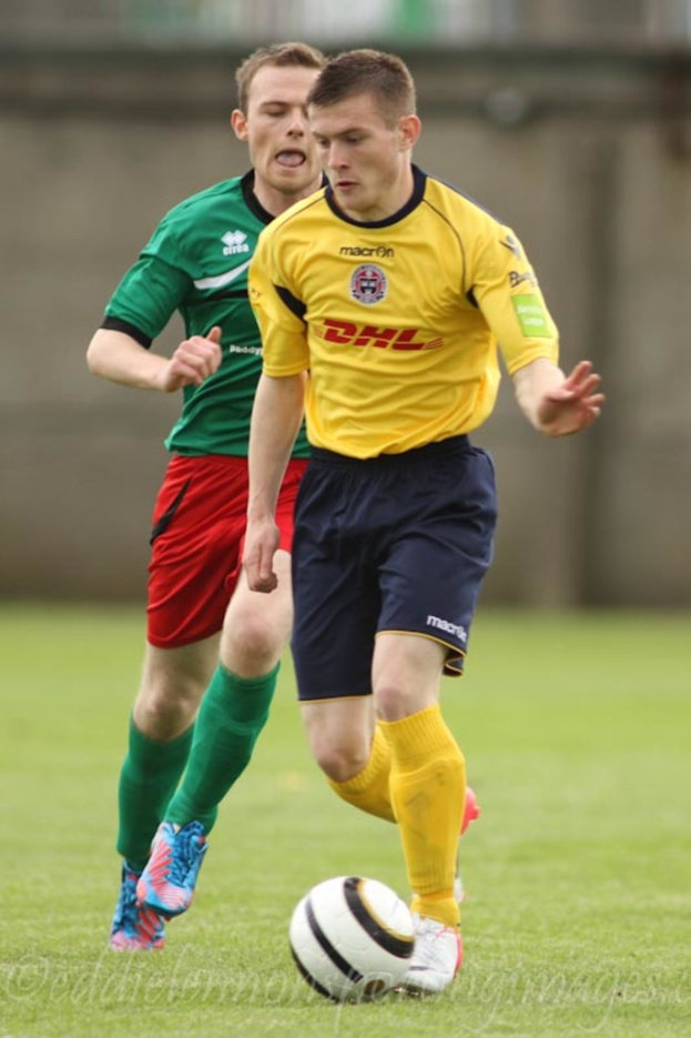 Zwei Männer spielen Fußball auf einem grünen Rasen mit einem Ball, mit unscharfem Hintergrund und Text unten.