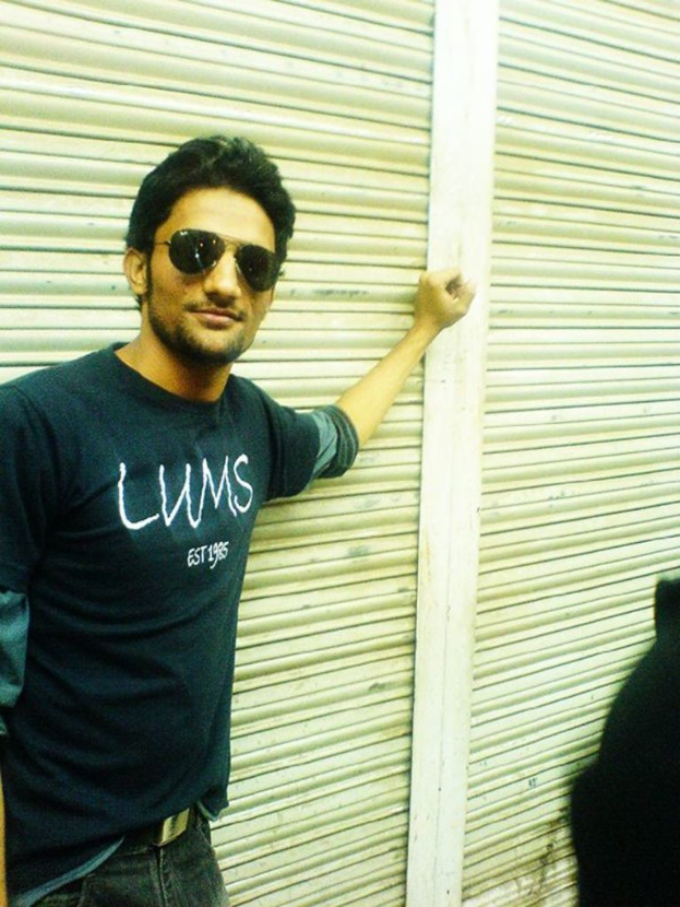 Ein Mann in einem T-Shirt, Hose und Brille steht neben einem Rollladen.