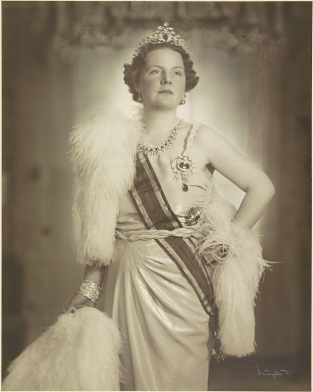 Schwarz-weiß-Foto von Queen Elizabeth II in einem Kleid und einer Krone, mit unscharfem Hintergrund und Text unten.