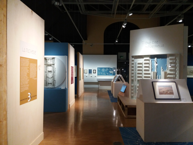 Ein Raum voller verschiedener Kunstwerke, darunter gerahmte Fotos auf Tischen, Texttafeln an den Wänden, Deckenbeleuchtung und ein Teppichboden, präsentiert eine Ausstellung im Museum of Modern Art.