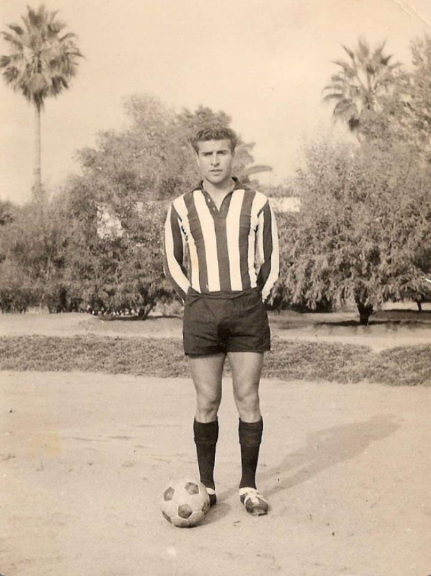 Ein Schwarz-Weiß-Foto eines alten Mannes mit einem Fußball, mit Bäumen und Himmel im Hintergrund.