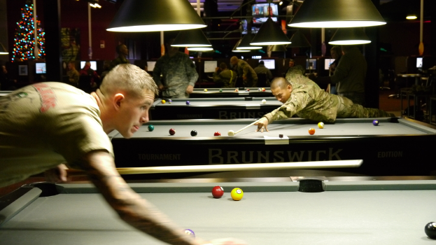 Ein Raum mit Snookertischen, Spielern auf beiden Seiten, hÃ¤ngenden LÃ¤mpchen, einem Weihnachtsbaum in einer Ecke und Bildschirmen mit PunktestÃ¤nden.