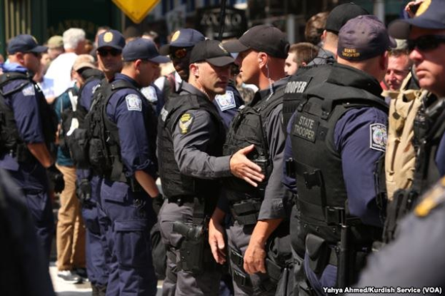 Gruppe von Polizisten in Uniform auf einer Straße mit Gebäuden und Schildern im Hintergrund, einige halten Schusswaffen.
