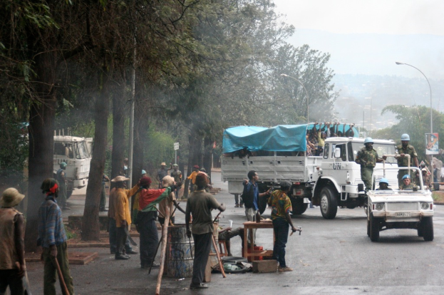 Arbeiter führen Aufgaben neben einer Straße mit einem Lastwagen durch, auf dem eine große Menge Menschen steht, während Beamte in einem Fahrzeug in der Nähe fahren, umgeben von Bäumen und Straßenlaternen.