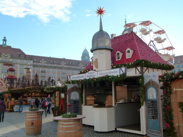 Ein lebendiger Weihnachtsmarkt in N├╝rnberg, Deutschland, mit Menschen um dekorierte St├Ąnde, Geb├Ąude, ein Riesenrad und einen bew├Âlktem Himmel, mit einer Tafel auf der rechten Seite.