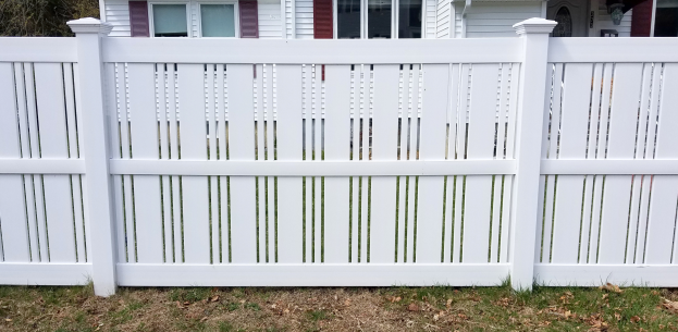 Eine weiße Vinyl-Privatsicherheitszäunung steht vor einem Haus mit Fenstern, umgeben von Gras und trockenen Blättern, mit Bäumen im Hintergrund.