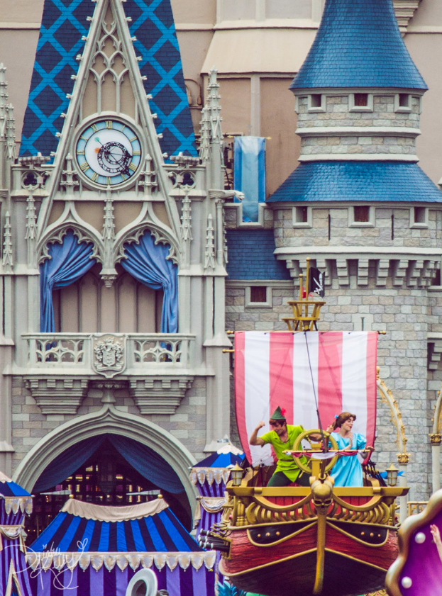 Eine bootähnliche Struktur auf der rechten Seite mit tanzenden Menschen und einer Fahne, mit einem Gebäude mit Uhr und Vorhängen im Hintergrund.