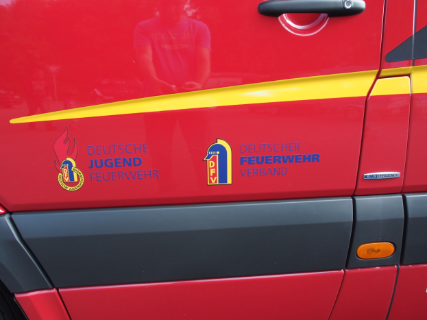 Roter Van mit einer gelben Streifen, Türgriff und einem schildförmigen Logo mit einem Löwen in einem Lorbeerkranz, beschriftet mit "Deutscher Jugendfeuerwehrverband".