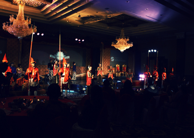 Eine Gruppe von Menschen, die in einem Auditorium eine Vorstellung anschauen, mit zwei Kronleuchtern an der Decke.