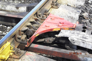 Nahaufnahme einer Schiene mit einem Metallschutz und Schottersteinen.