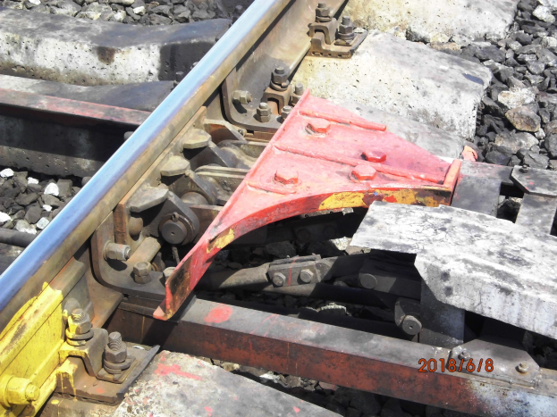 Nahaufnahme einer Schiene mit einem Metallschutz und Schottersteinen.