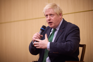 Ein Mann im Anzug und Krawatte sitzt auf einem Stuhl und hält ein Mikrofon, scheinbar mitten in einer hitzigen Diskussion.