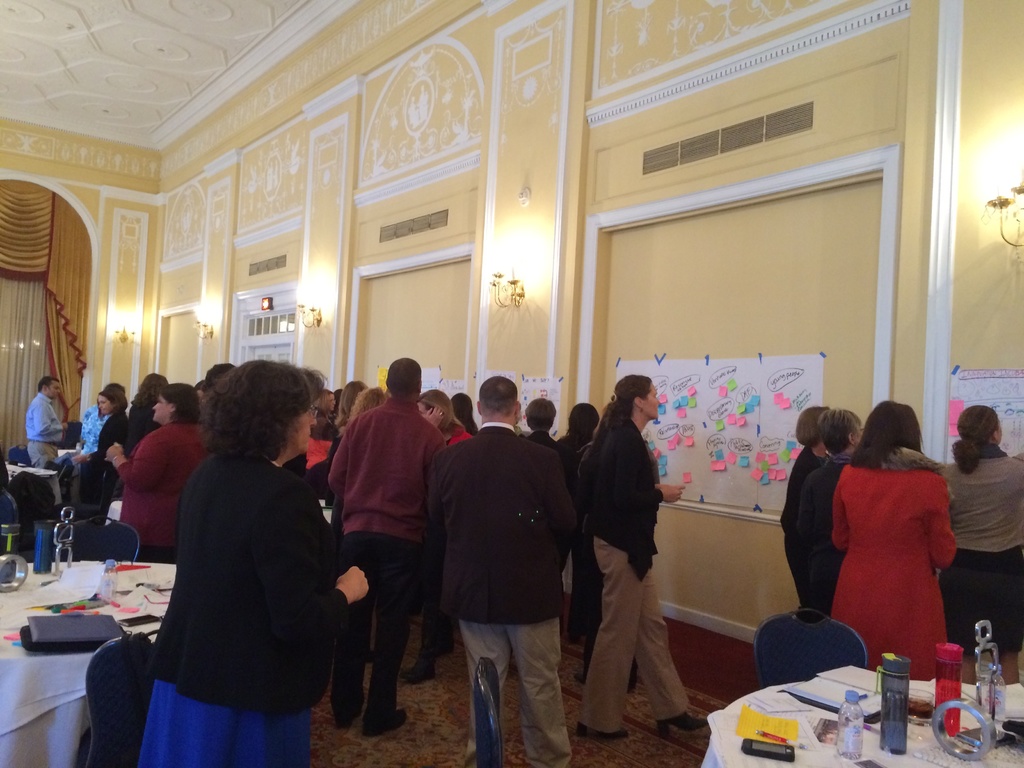 Eine Gruppe von Menschen untersucht Plakate und Diagramme, die an einer Wand in einem Gebäude zu sein scheinen.