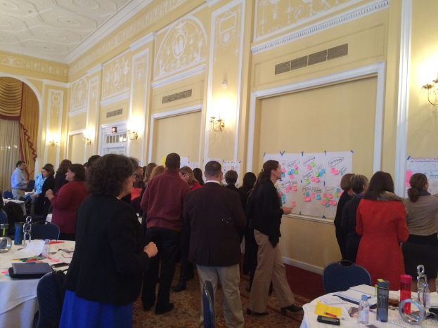 Eine Gruppe von Menschen untersucht Plakate und Diagramme, die an einer Wand in einem Gebäude zu sein scheinen.