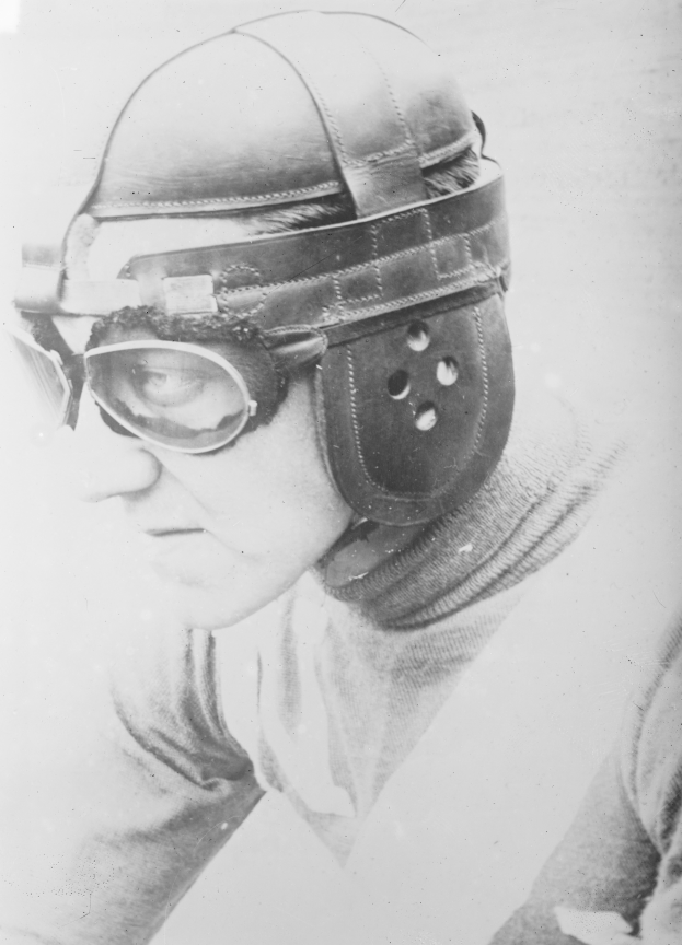 Ein Mann in einem Helm und Brillengläsern, mit einem ernsten Gesichtsausdruck, schaut konzentriert in die Ferne auf einem alten Schwarz-Weiß-Foto.