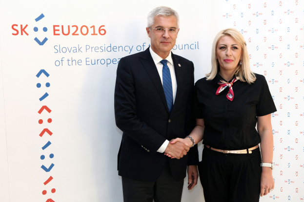 Zwei Personen, der Präsident des Europäischen Rates, stehen strahlend nebeneinander vor einer Tafel mit der Aufschrift "sk eu 2016"; der Mann trägt eine schwarze Jacke, ein weißes Hemd, eine blaue Krawatte und schwarze Hosen, die Frau trägt eine Brille.