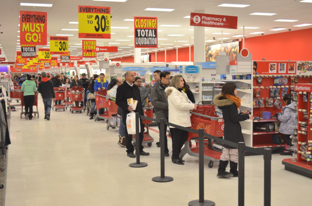Eine große Gruppe von Menschen beim Einkaufen in einem Walmart-Geschäft während des Black Friday, mit Einkaufswagen, Taschen, Stangen mit Bändern, Regalen, Informationsschildern und Deckenleuchten.